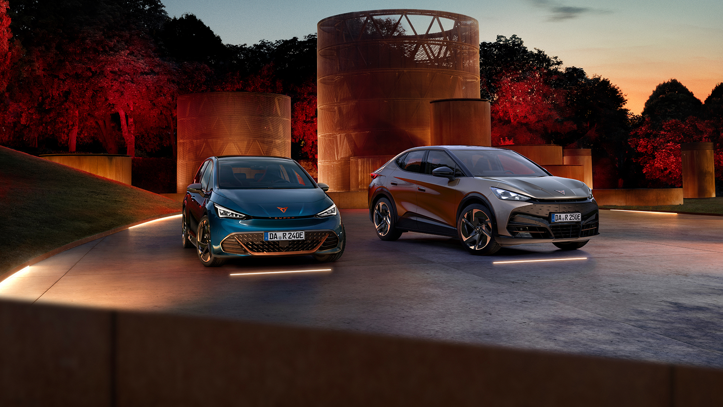 CUPRA Born und CUPRA Tavascan nebeneinander auf einer beleuchteten Fläche vor architektonischem Hintergrund